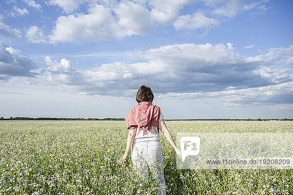 Woman walking in rapeseed field under cloudy sky