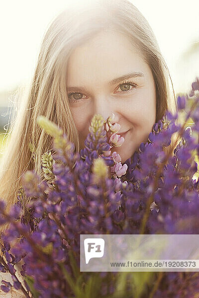 Smiling blond woman with bunch of purple lupine flowers on sunny day