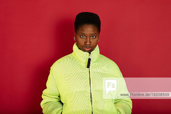 Woman wearing green jacket standing against red background