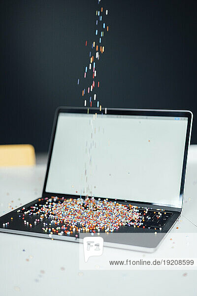 Multi colored pearls falling on laptop at desk