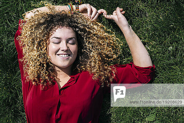 Smiling woman with curly hair lying on grass