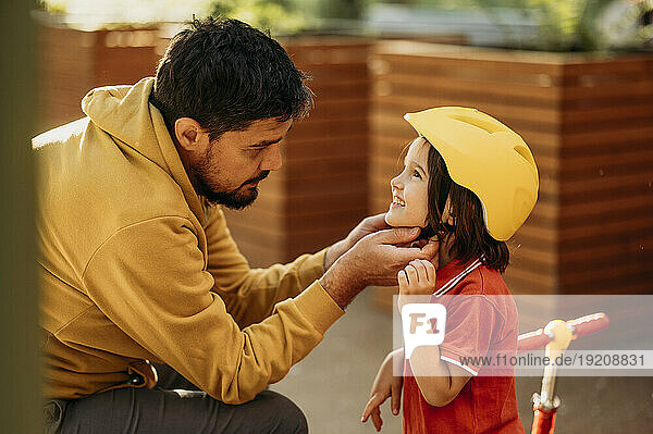 Father tying helmet on smiling son
