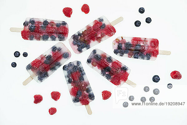 Studio shot of homemade popsicles with fresh raspberries  blueberries and gooseberries lying against white background