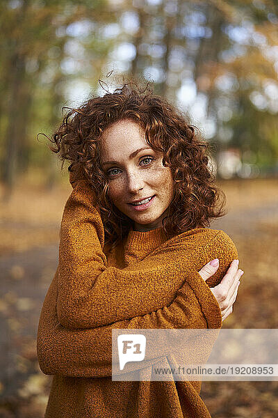 Smiling redhead woman wearing sweater at autumn park
