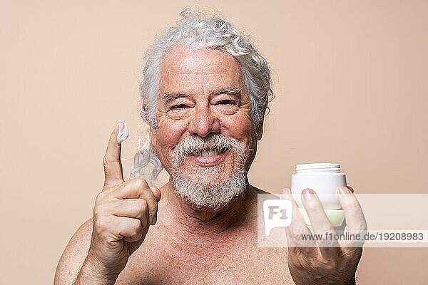 Smiling man with moisturizer on finger against beige background