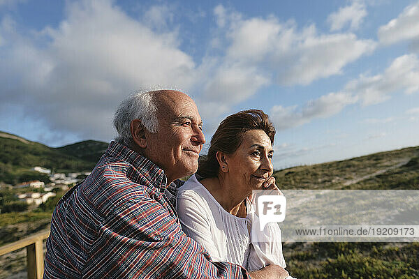 Smiling senior man and woman under cloudy sky on sunny day