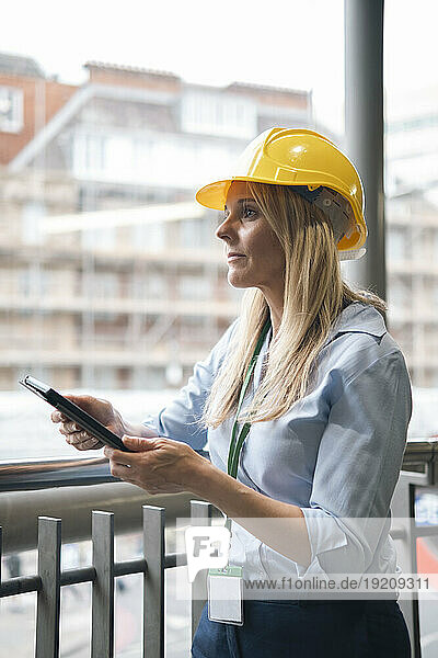 Contemplative businesswoman holding tablet PC leaning on railing