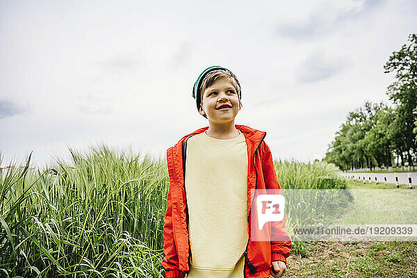 Smiling boy wearing red jacket standing by barley crop on field