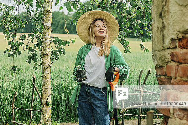 Smiling woman holding potted plant in garden