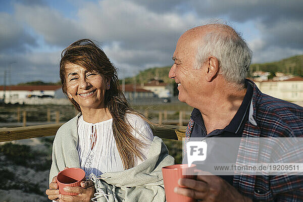 Happy senior woman and man holding coffee cups under cloudy sky