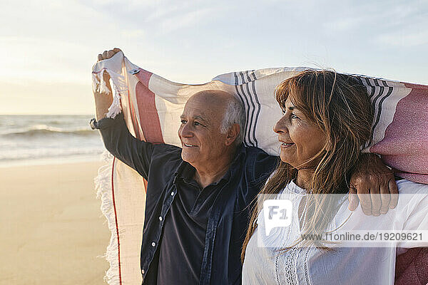 Happy senior couple holding scarf at beach