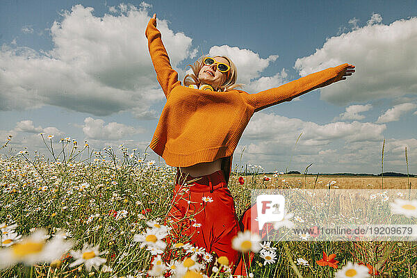 Carefree woman jumping with arms raised in chamomile field