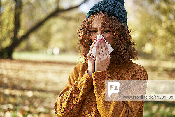 Redhead woman blowing nose with facial tissue at autumn park
