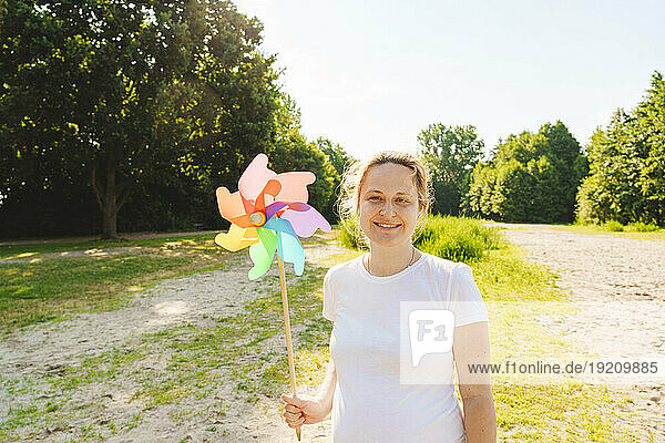 Smiling pregnant woman holding rainbow pinwheel toy on field