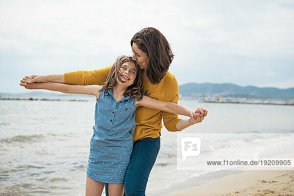 Happy mother embracing and kissing daughter in front of sea at beach