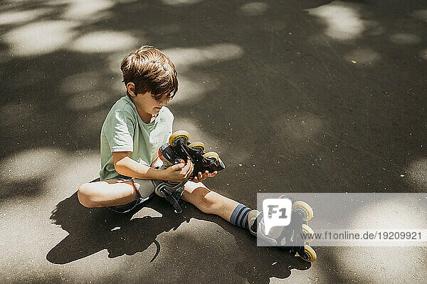 Boy removing inline skates sitting on footpath