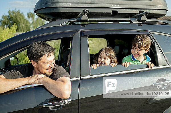 Happy father with children looking through car window on sunny day