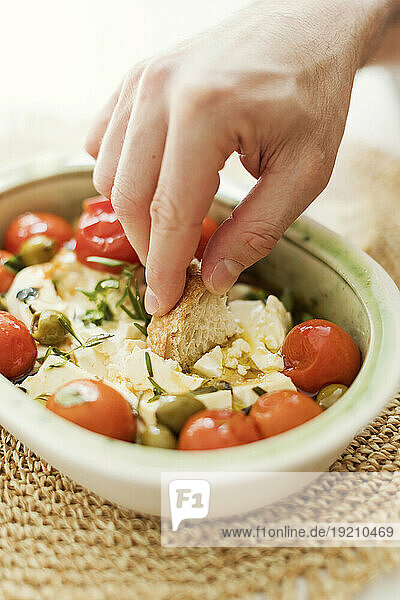 Hand of person eating baked feta cheese with olives  cherry tomatoes and herbs