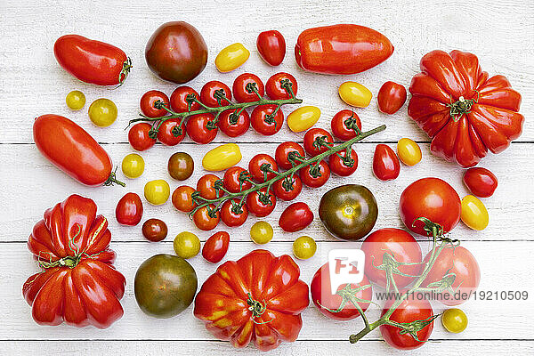 Different varieties of ripe tomatoes flat laid against white wooden surface