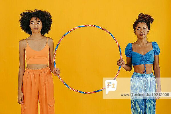 Young friends holding plastic hoop against yellow background
