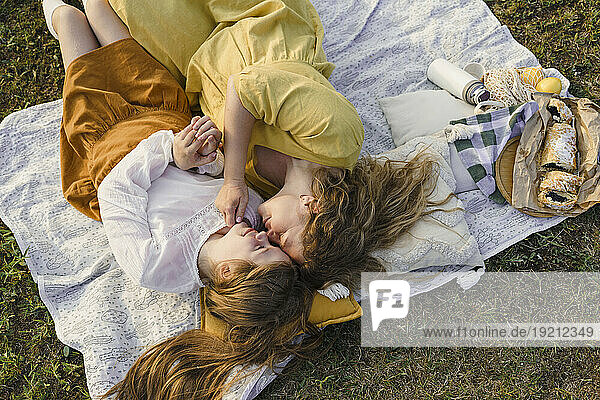 Mother and daughter rubbing noses and lying on picnic blanket