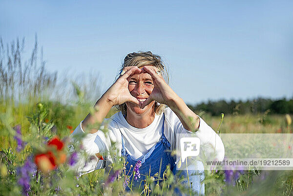 Happy woman making heart gesture sitting in meadow