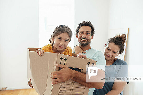 Happy man and woman with daughter sitting in cardboard box at home