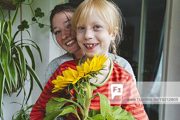 Teenage girl with blond sister holding sunflower on balcony