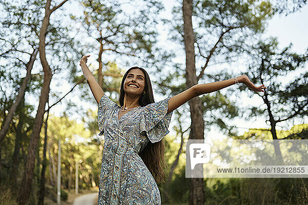Happy teenage girl with arms outstretched in forest at sunset