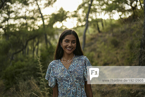 Smiling teenage girl standing in forest at sunset