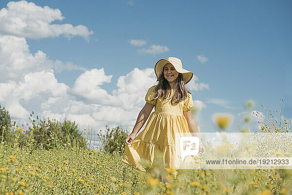 Smiling girl wearing hat and standing in flower field