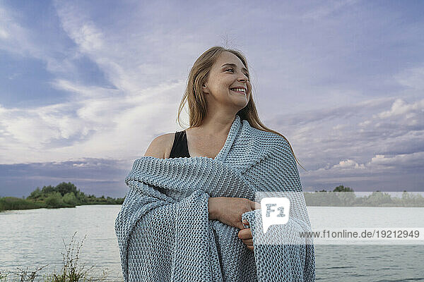 Smiling woman wrapped in woolen scarf standing near lake