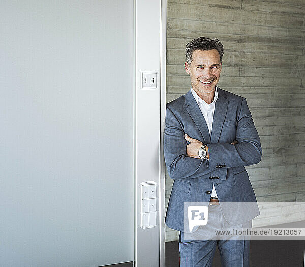Happy businessman standing with arms crossed in front of wall