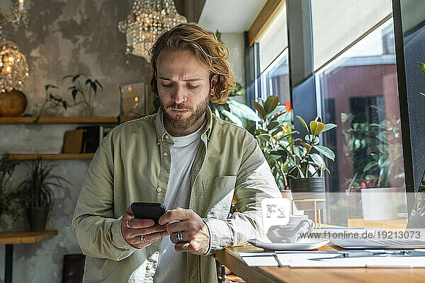 Businessman using smart phone leaning on desk at cafe