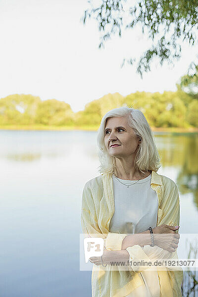 Mature woman hugging self in front of lake