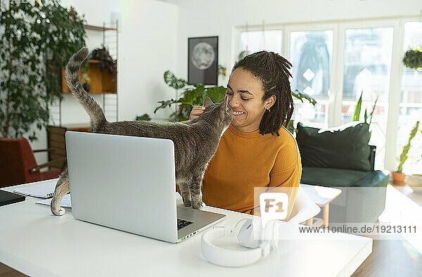 Smiling freelancer with laptop and cat at desk in home office