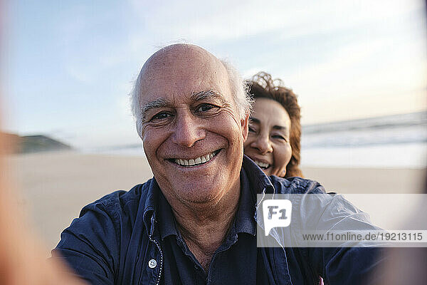 Happy senior man taking selfie with woman at beach