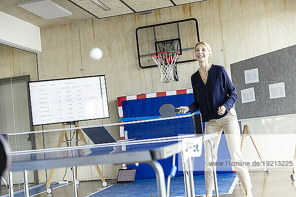 Happy mature businesswoman playing tennis in office