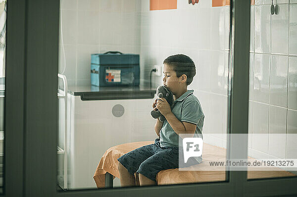 Worried boy sitting with stuffed toy at medical clinic