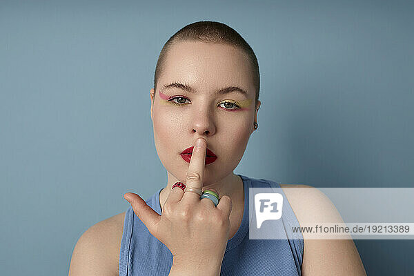 Rude woman with middle finger on lips against blue background