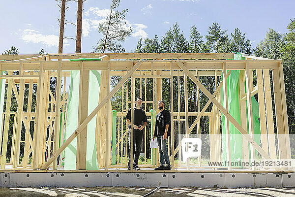 Engineers standing with blueprint near wooden frame on sunny day