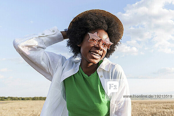 Happy afro woman wearing hat and star shape sunglasses in field