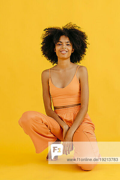 Smiling woman kneeling against yellow background
