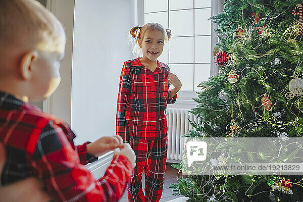Smiling sister looking at brother near Christmas tree at home