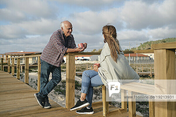 Happy senior couple with coffee cups spending time together on boardwalk