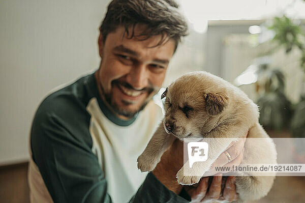 Happy man holding mixed breed puppy at home