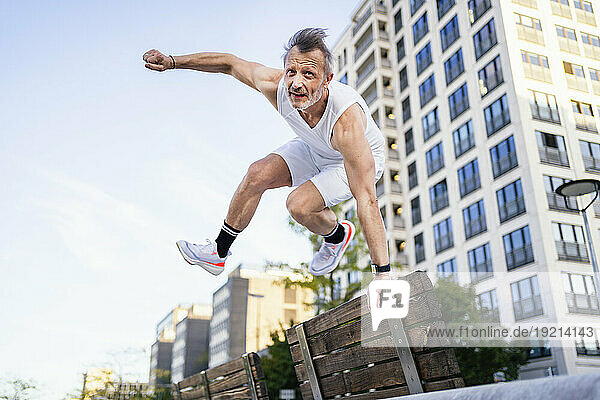 Active athlete jumping over bench in city