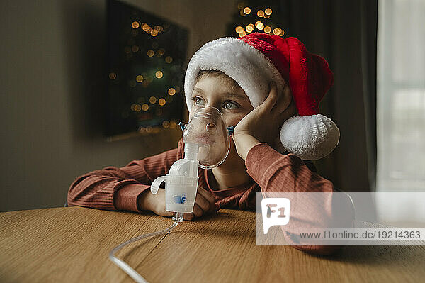 Contemplative boy using inhaler sitting at table
