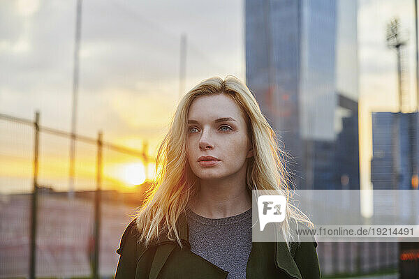 Thoughtful blond woman walking in city at sunset