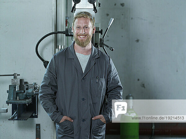 Smiling blue-collar worker standing with hands in pockets at factory